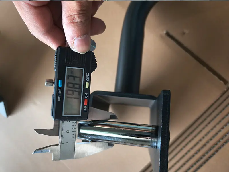 Digital caliper measuring the metal pin diameter of a gym equipment accessory during quality inspection.