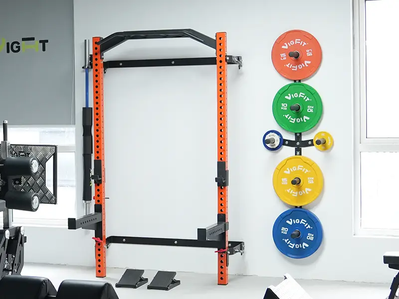 Orange wall-mounted folding squat rack with pull-up bar, spotter arms and wall-mounted weight plate storage.