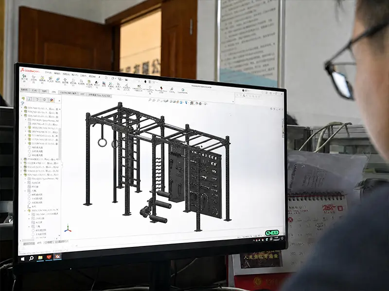 CAD model of a functional training rig with gymnastic rings, a climbing ladder and attachment panels displayed on a computer screen