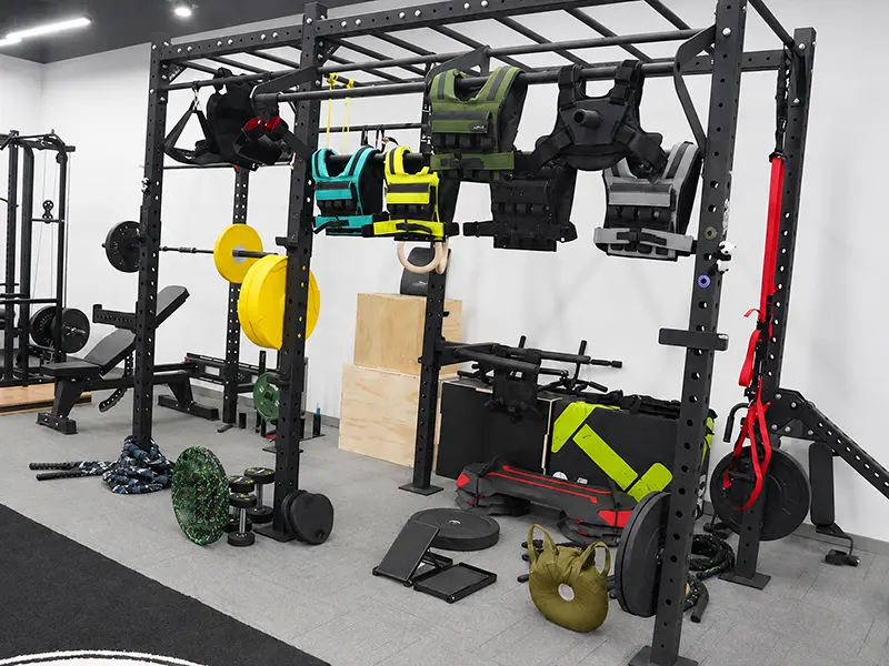 Commercial functional training rig displayed with weighted vests, weight plates, kettlebells and training attachments.