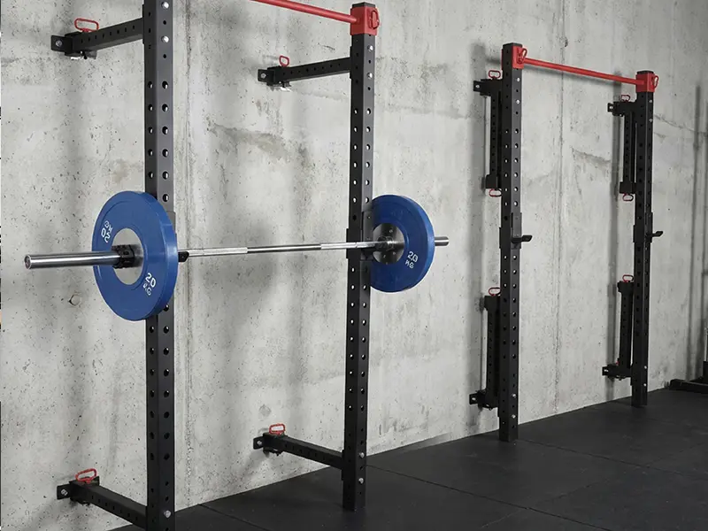 Wall-mounted folding squat racks with pull-up bars, J-hooks and a loaded Olympic barbell.