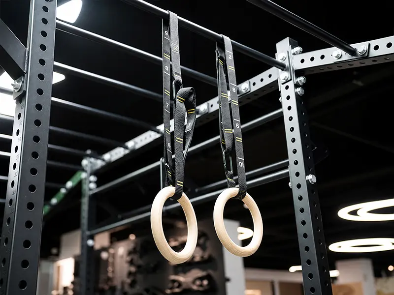 Wooden gymnastic rings with numbered adjustable straps hanging from a functional training rig