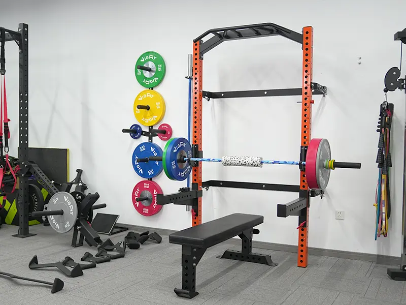 Orange wall-mounted folding squat rack with pull-up bar, spotter arms, weight bench and loaded barbell.